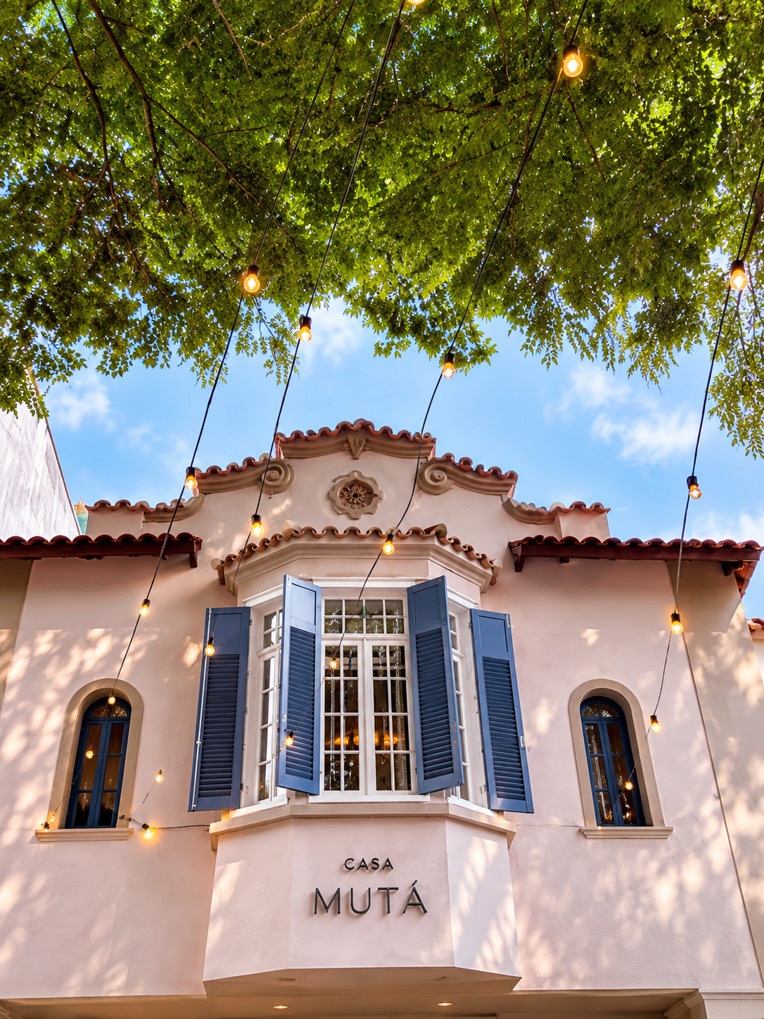 Fachada da Casa Mutá, com janelas azuis e árvores